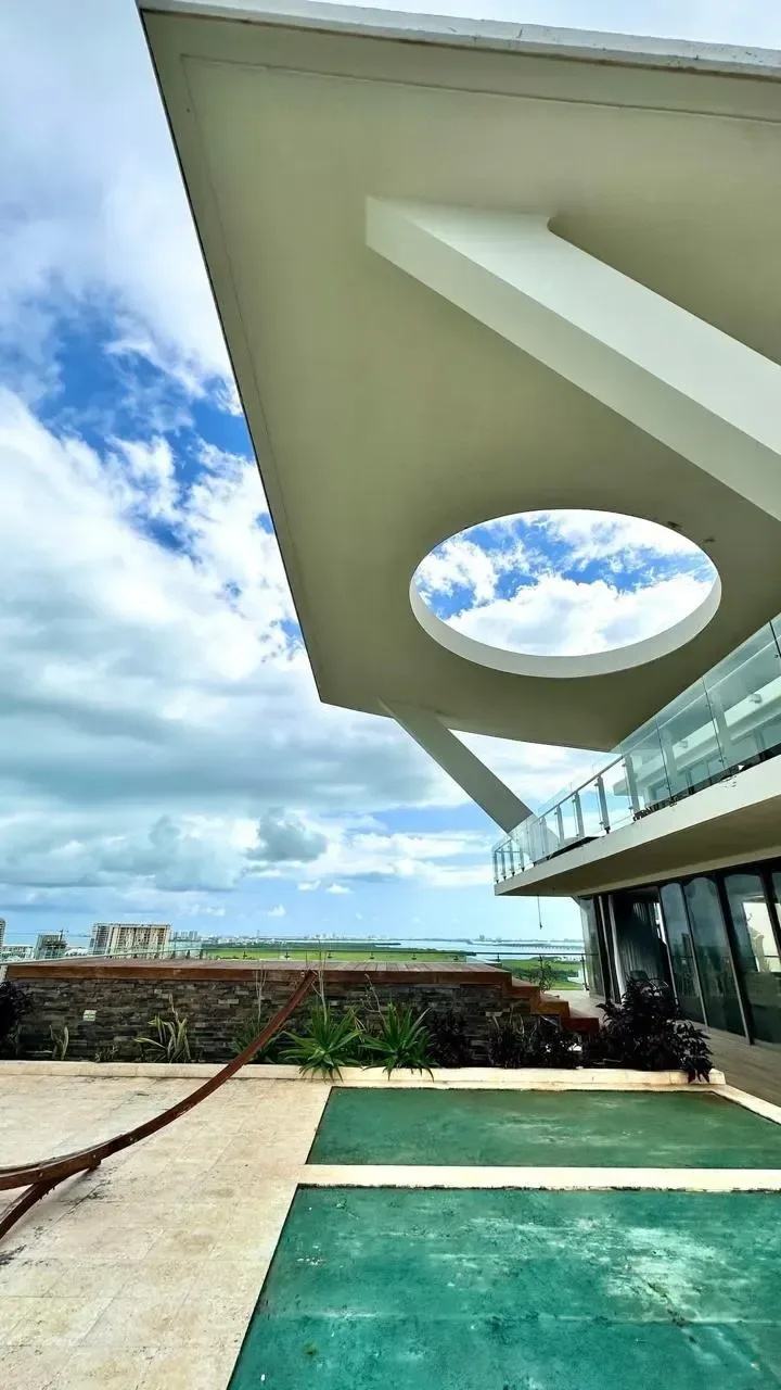 Terrace with a white roof and a circular opening framing the sky; balcony edge and paved areas visible in the foreground.